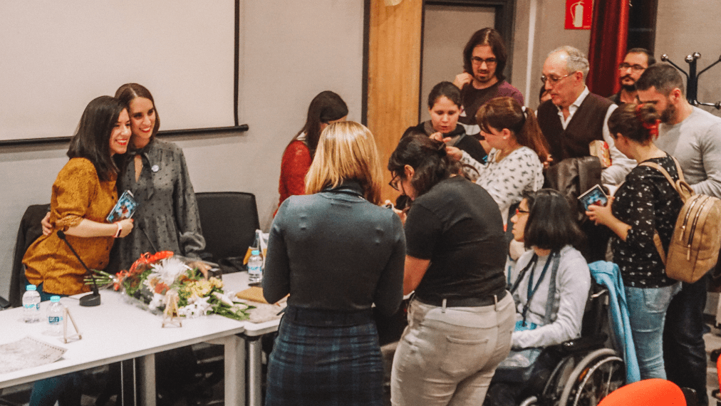Fotografía realizada durante la presentación de 'El último de los thaûrim' en la que estoy posando con Sonia Lerones detrás de la mesa y se ve un grupo de gente esperando para que la firma